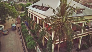 Un edificio de varios pisos con techo inclinado, rodeado de vegetación y vehículos estacionados.