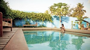 Una piscina con muelle de madera, una banca y una persona leyendo un libro.