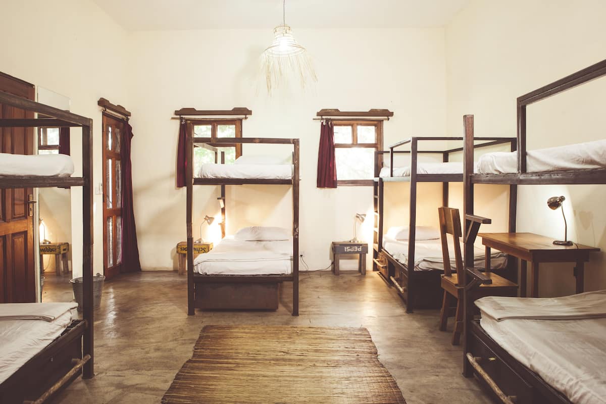 A dormitory room with bunk beds, a desk, a chair, and a hanging light fixture.