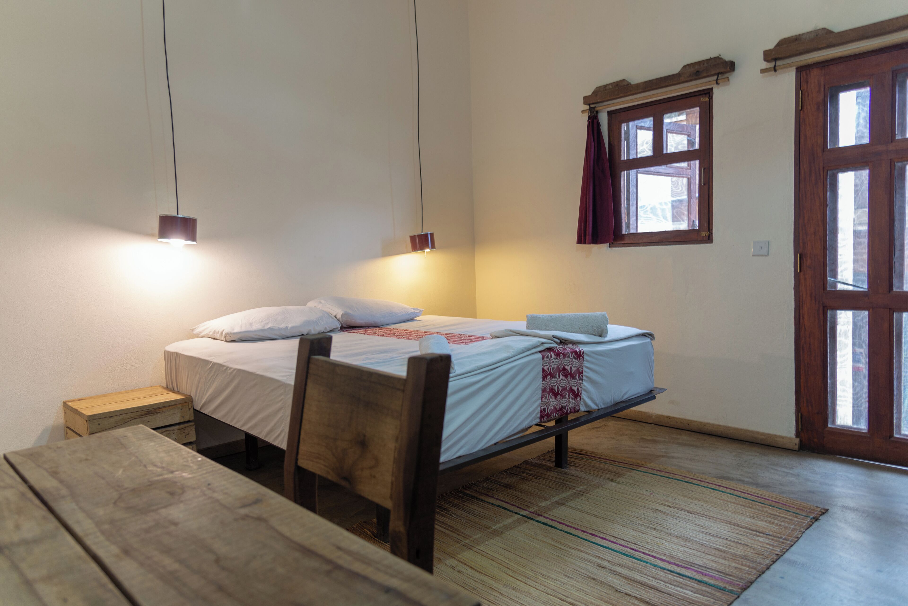 Une petite chambre à coucher, chaleureuse et accueillante, avec un lit simple, une table de chevet en bois, une petite table et une fenêtre avec des rideaux.