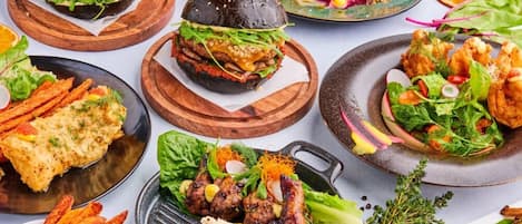Diversos platos que incluyen hamburguesas, pollo a la parrilla y ensaladas, presentados en tablas y platos de madera.