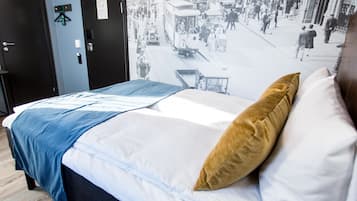 A bed with a blue and white bedspread, a brown pillow, and a wall with a vintage street scene.