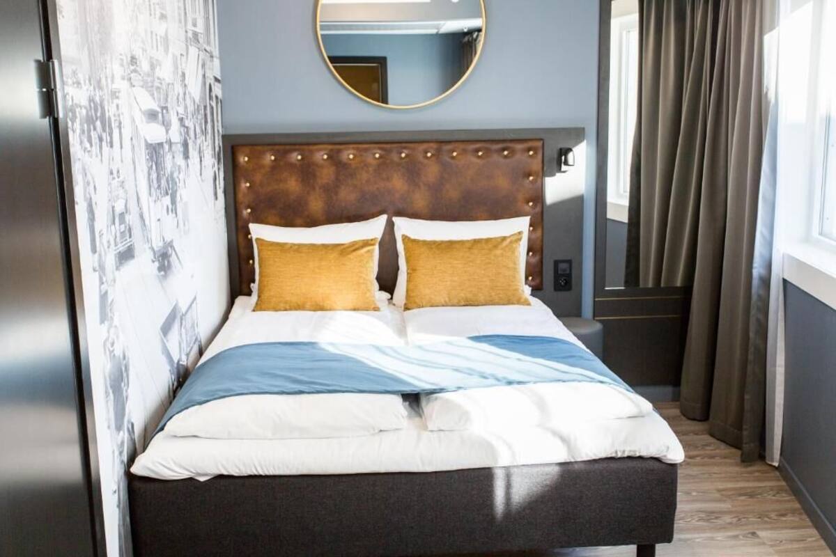 A neatly made bed with a headboard, a mirror above it, and a window with curtains.