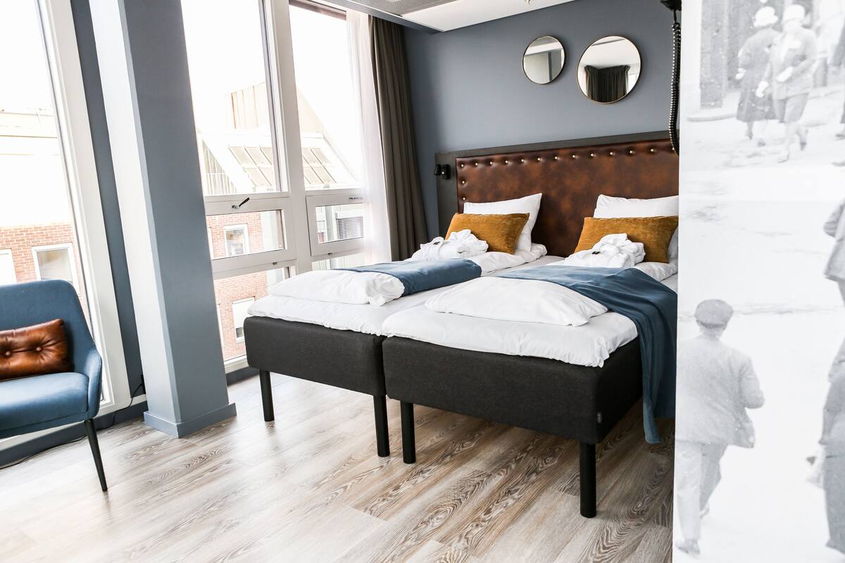 A modern hotel room with a large bed, a blue chair, and a view of the outside.