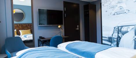 Habitación de hotel con cama, escritorio, silla, televisor y espejo.