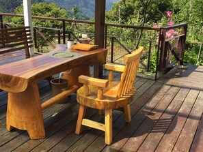 A wooden deck with a table and chairs, surrounded by a metal railing and lush greenery. - Sunrise235 (Zhuqi)
