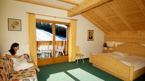 A cozy room with a wooden bed, a sofa, and a view of a snowy landscape through a glass door. - Hotel Jú Furcia (Marebbe)