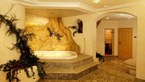 A spa area with a hot tub, stone steps, and a wooden door. - Hotel Jú Furcia (Marebbe)
