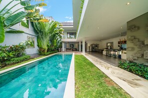Un espace piscine moderne avec une piscine à eau claire, entouré d’une végétation luxuriante et d’une pelouse bien entretenue.