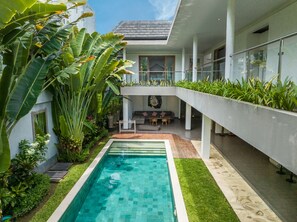 Un espace piscine extérieur moderne, doté d’une piscine à l’eau d’un bleu limpide, entouré d’une végétation luxuriante et présentant un design architectural contemporain.