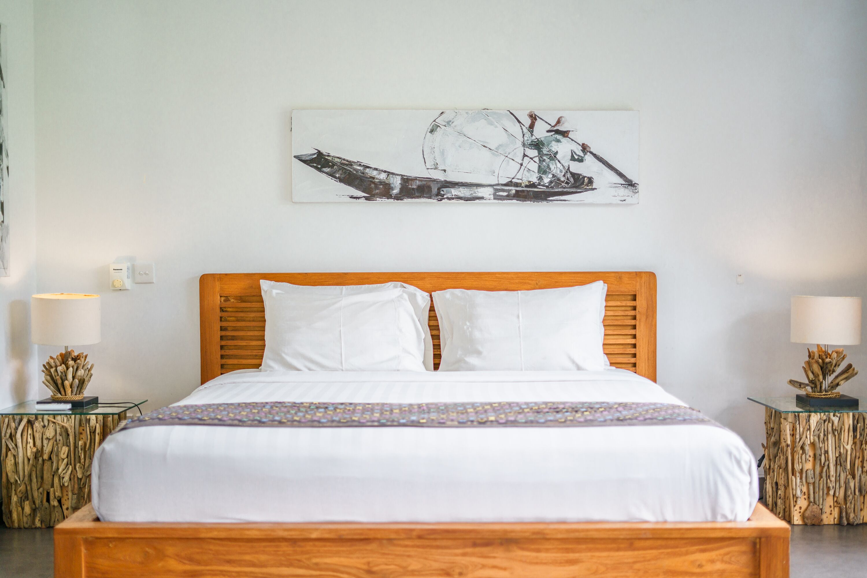 A neatly made bed with white linens, a wooden headboard, and two nightstands with lamps and decorative items.