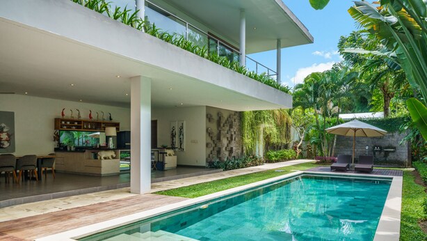 Un área de piscina moderna al aire libre con piscina cristalina, terraza de madera y zona de comedor con sillas y una mesa.