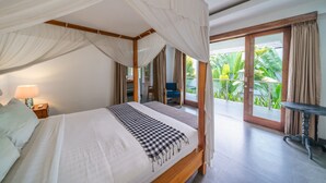Una cama con dosel, un plaid de cuadros, una mesita de noche con lámpara y vistas a un jardín exuberante a través de una puerta de cristal.