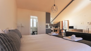Ein Hotelzimmer mit einem großen Bett, einer kleinen Küchenzeile, einem Spiegel und einer Hängelampe.