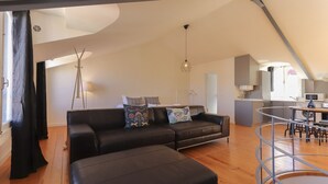 Ein modernes Wohnzimmer mit einer schwarzen Ledersofa, Holzboden und einem durchgehenden Durchgang zur Küche.
