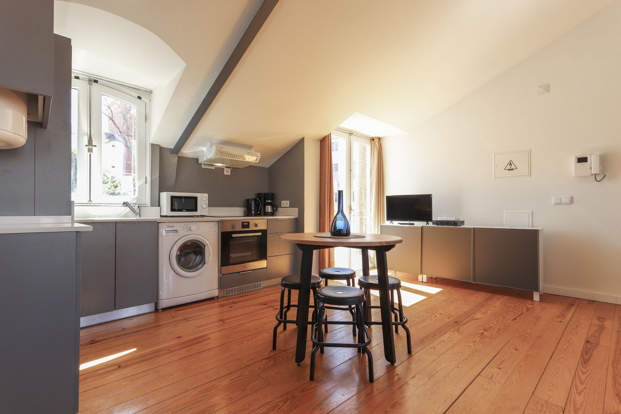 Une cuisine moderne équipée d’un lave-linge, d’un four et d’un four à micro-ondes. On y trouve également un coin repas avec des tabourets et une table.