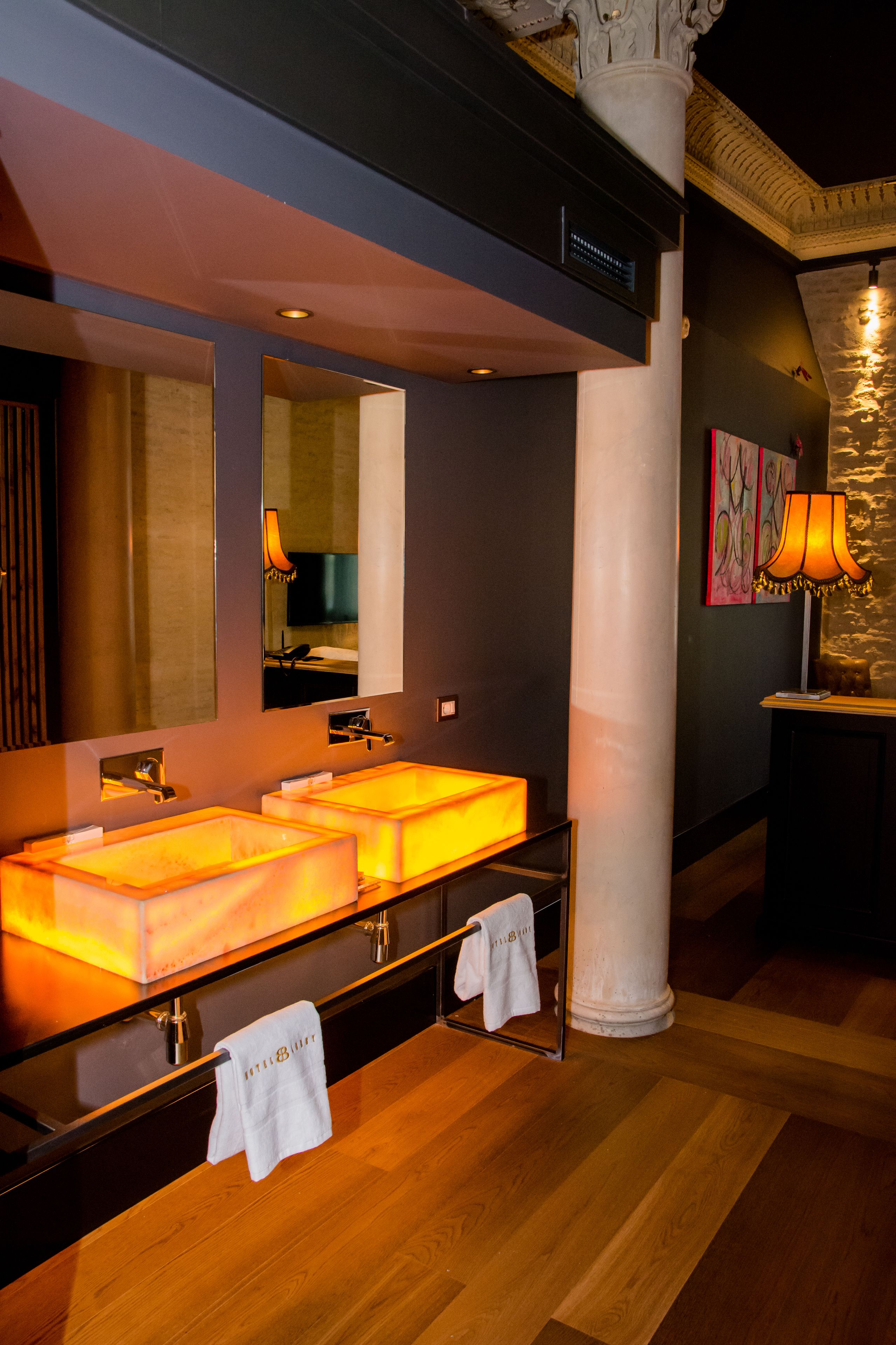 A modern bathroom with two illuminated sinks, a large mirror, and a stone wall.
