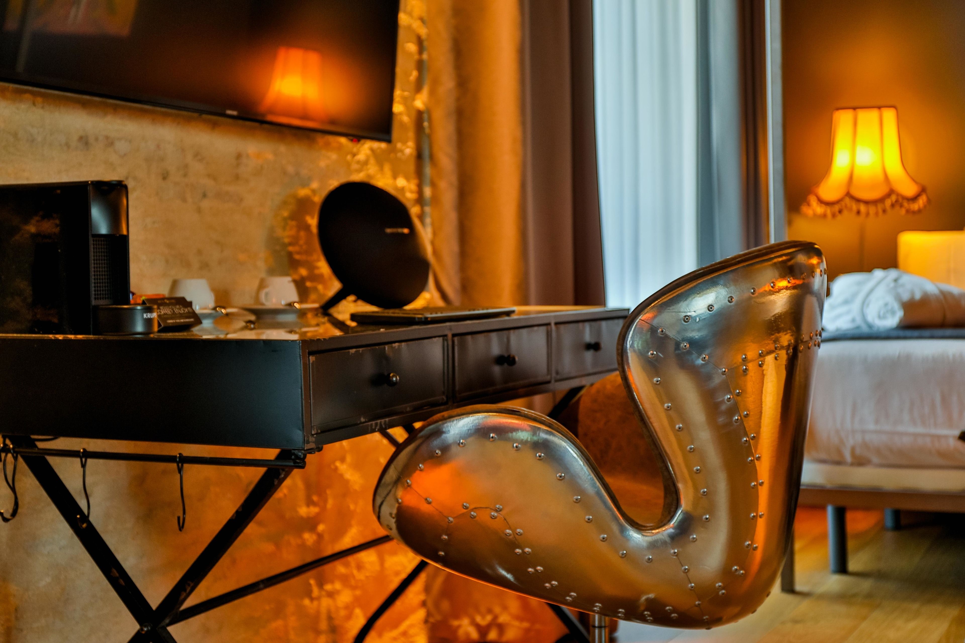 A modern room with a bed, a desk with a computer, and a unique metallic chair.