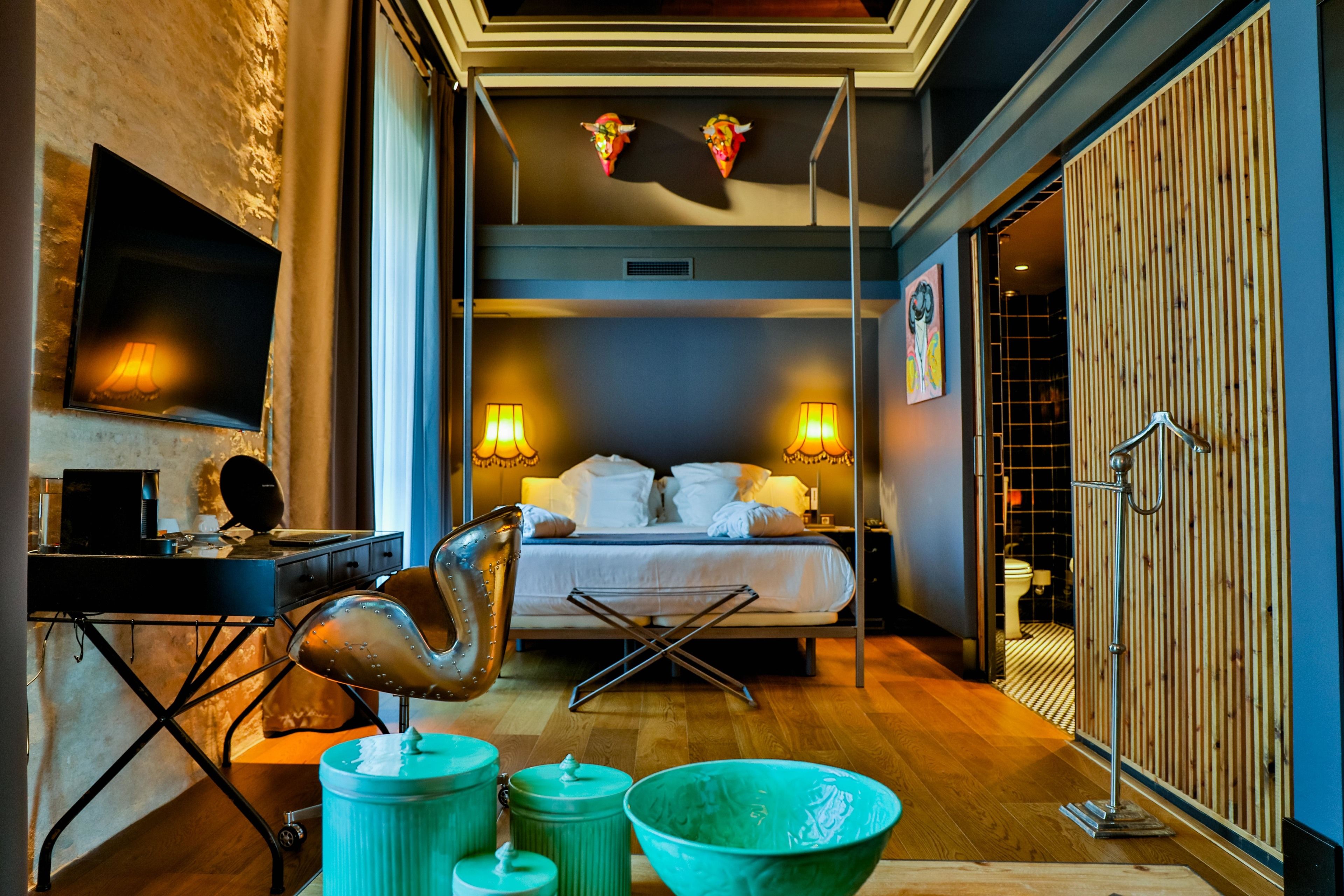 Una habitación de hotel moderna con una cama, lámparas de noche, un escritorio con una computadora y un tazón verde grande.