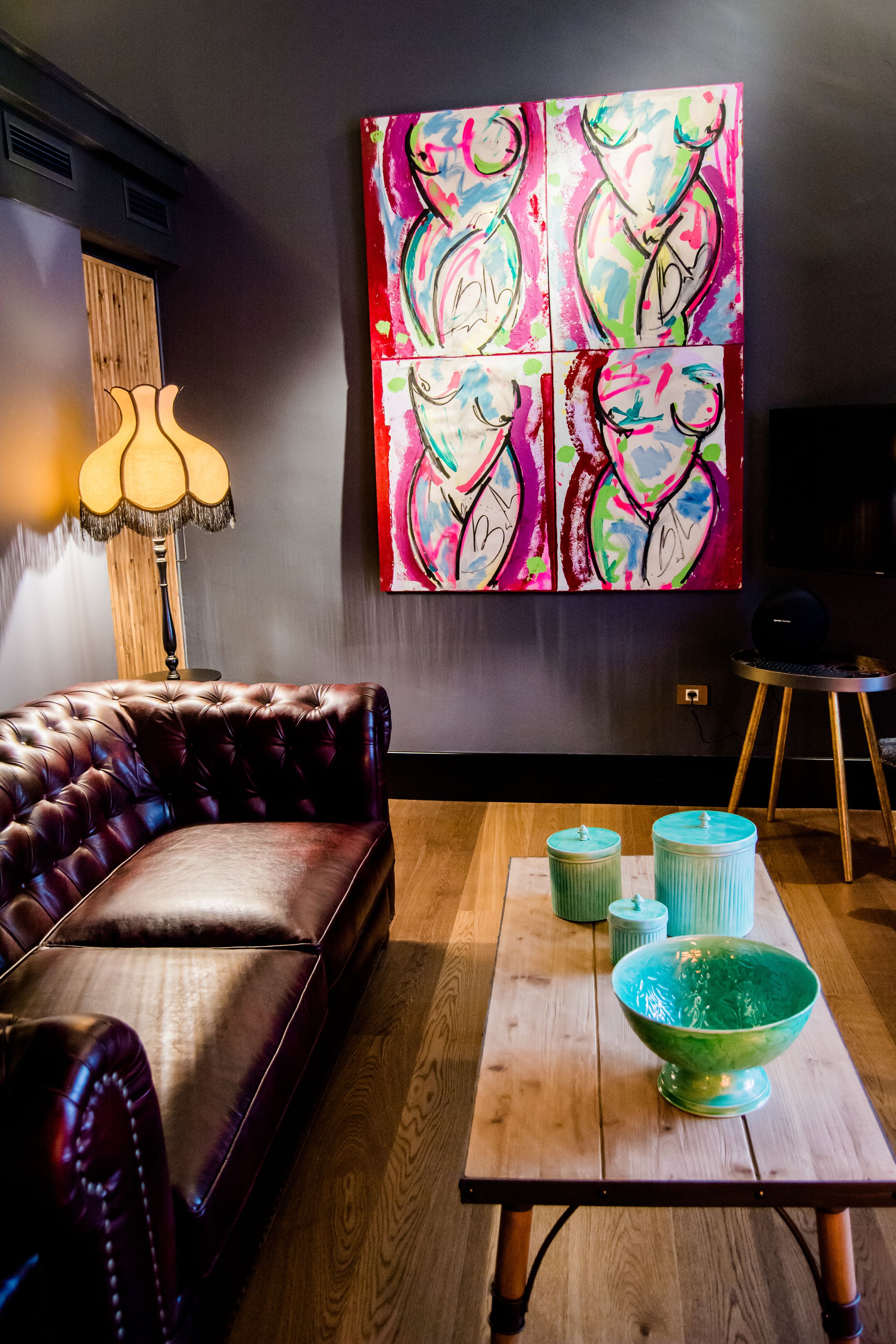 Una sala de estar con un sofá de cuero, una mesa de centro de madera con cuencos decorativos, un cuadro abstracto y colorido en la pared, y una lámpara.