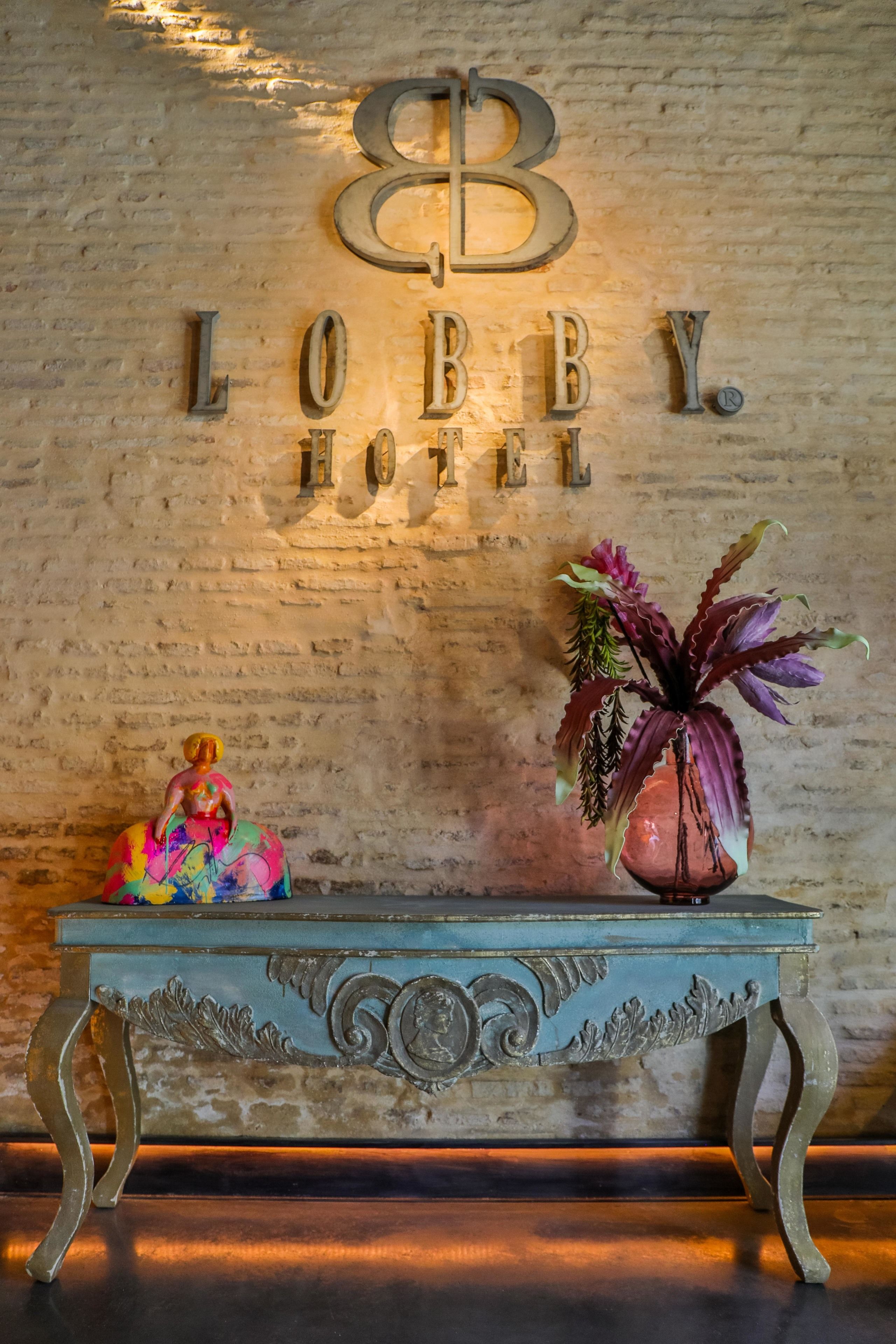 Un vestíbulo con un cartel que dice "LOBBY HOTEL", una mesa decorativa y un jarrón con flores.