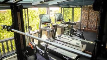 Uma academia com esteiras, máquinas de musculação e uma grande janela com vista para uma área verde.