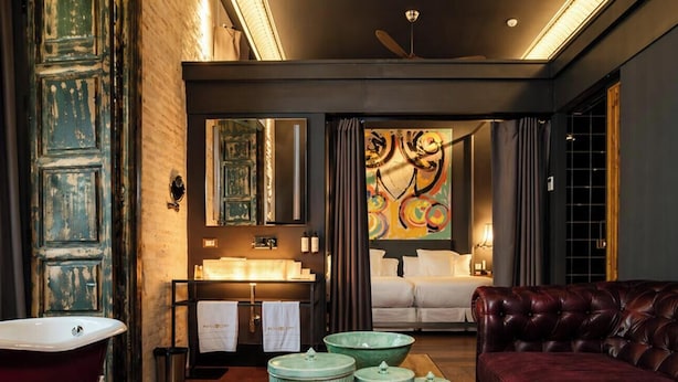 A room with a bathtub, a vanity with a mirror, a bed, and a leather armchair. - Hotel Lobby  (Seville)