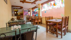 A dining area with wooden tables and chairs, a green marble table, and a window with colorful decorations.