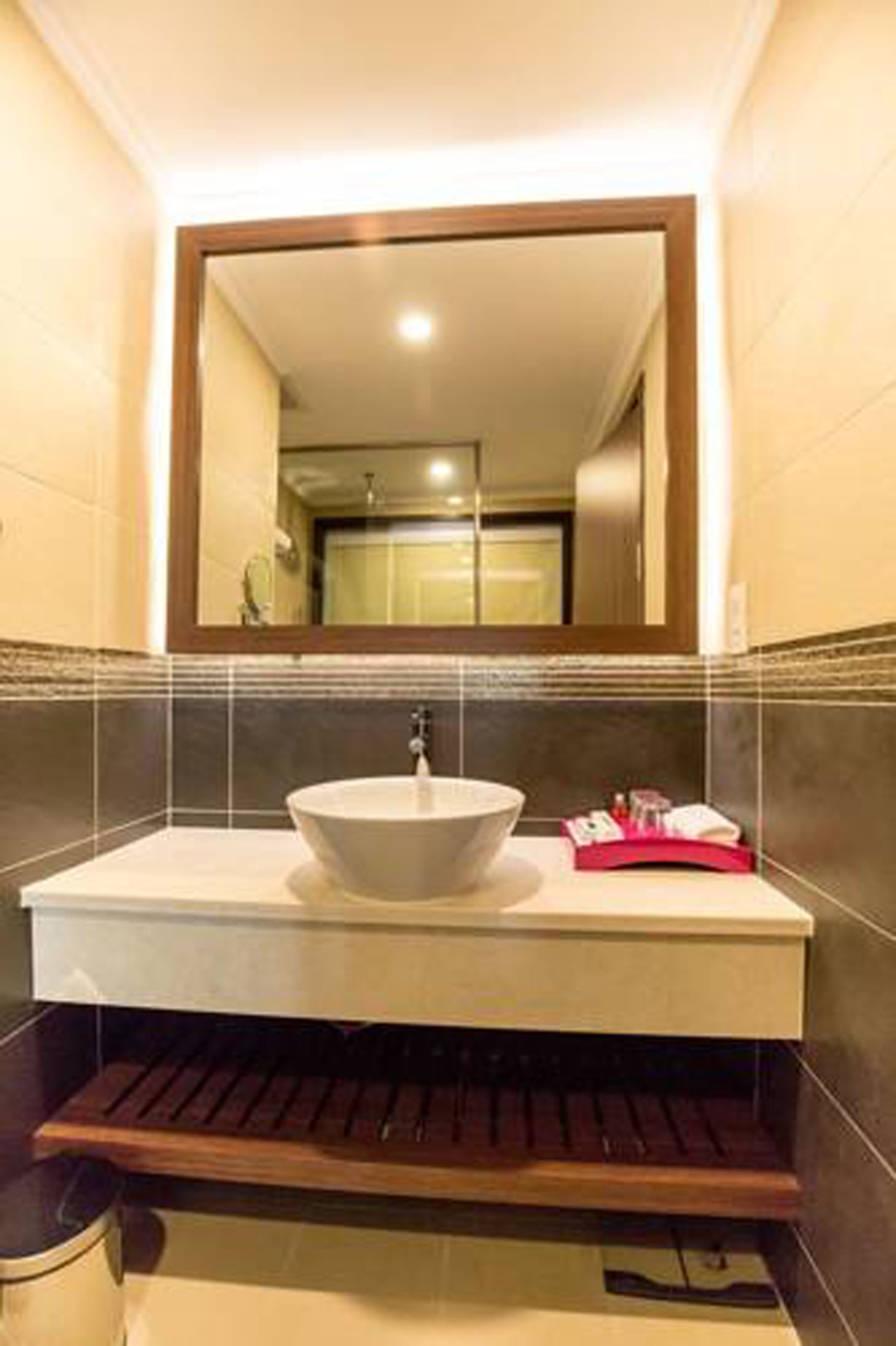 A bathroom with a large mirror, a vessel sink, and a wooden shelf.