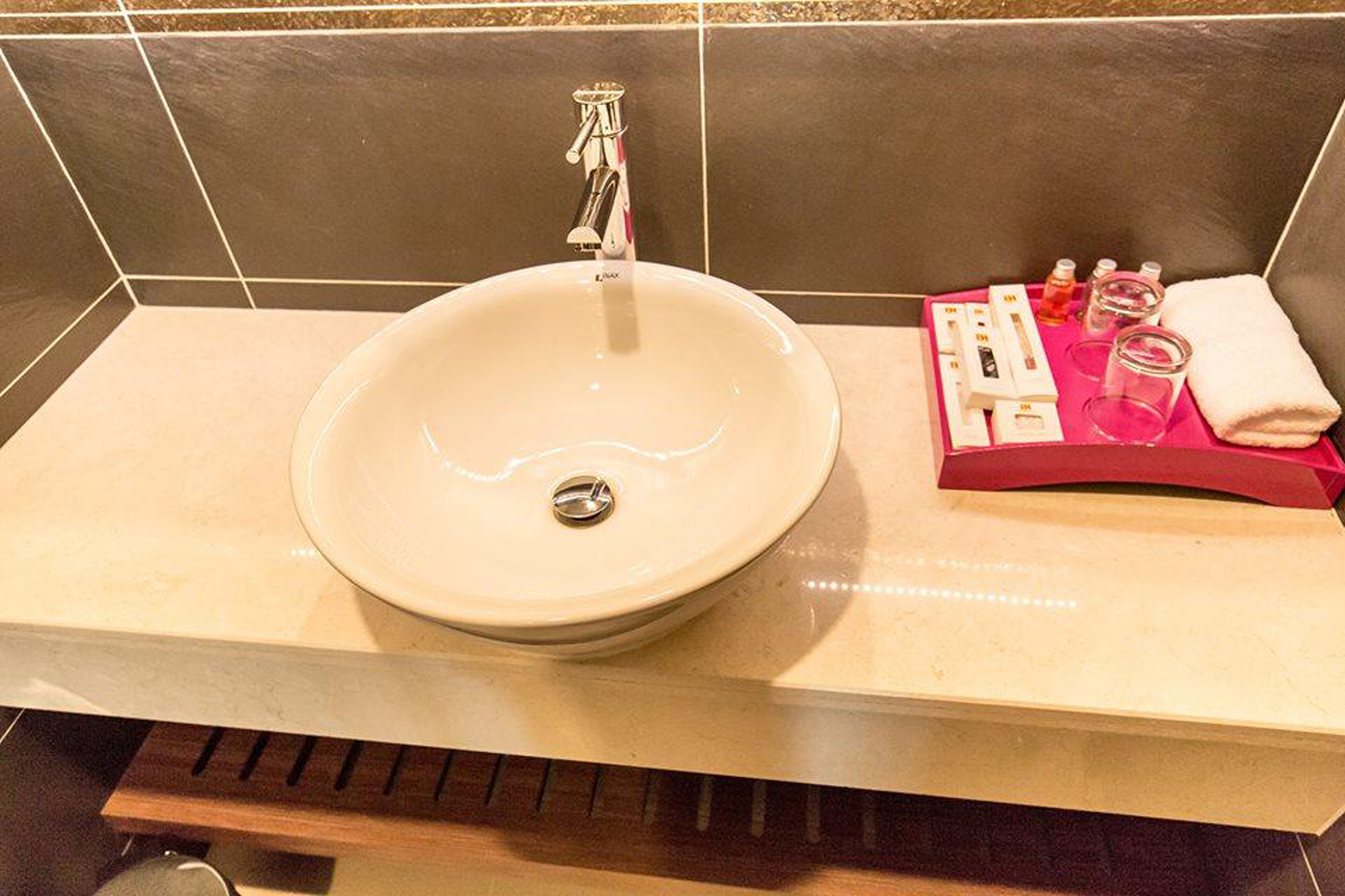 A bathroom with a large, round sink, a modern faucet, and a vanity area with toiletries and a towel.