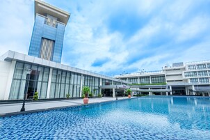 Un hotel moderno con una grande piscina, un edificio alto dal design originale e un cielo azzurro.
