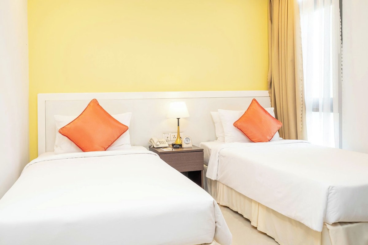 Une chambre d’hôtel avec deux lits, une table de chevet avec une lampe et une fenêtre avec des rideaux.