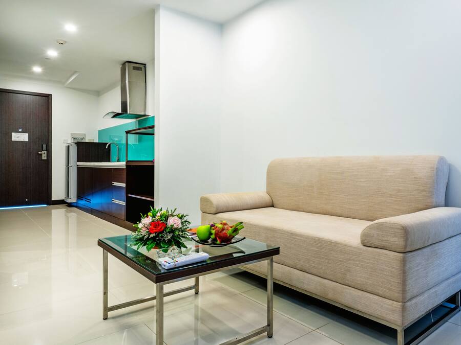 Un soggiorno moderno con un divano beige, un tavolino in vetro con un'esposizione floreale e un'area cucina sullo sfondo.