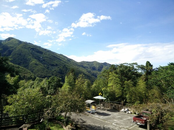 A parking area with a small pavilion, surrounded by lush greenery and mountains in the background.