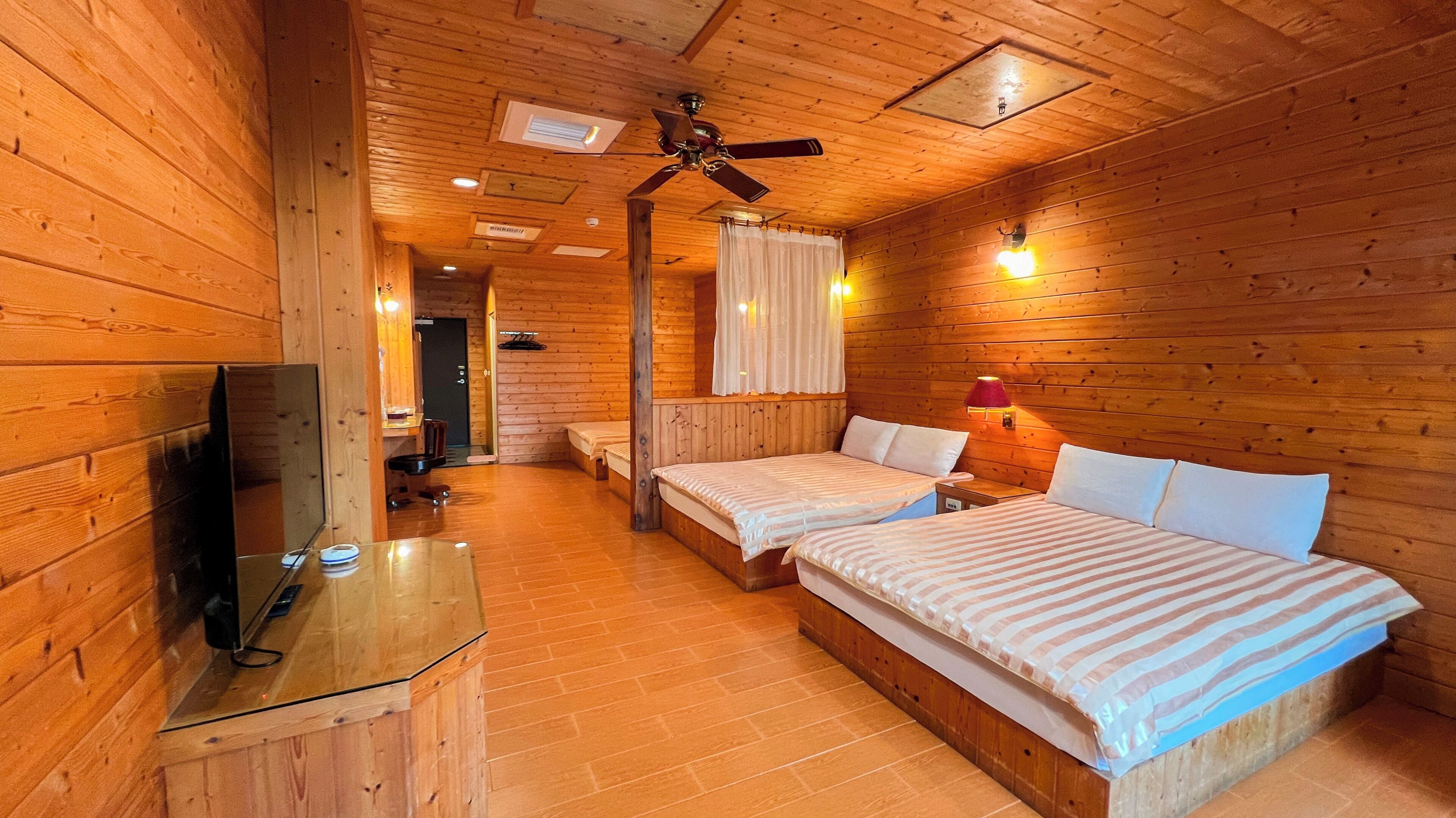 A wooden cabin room with two beds, a TV, and a ceiling fan.
