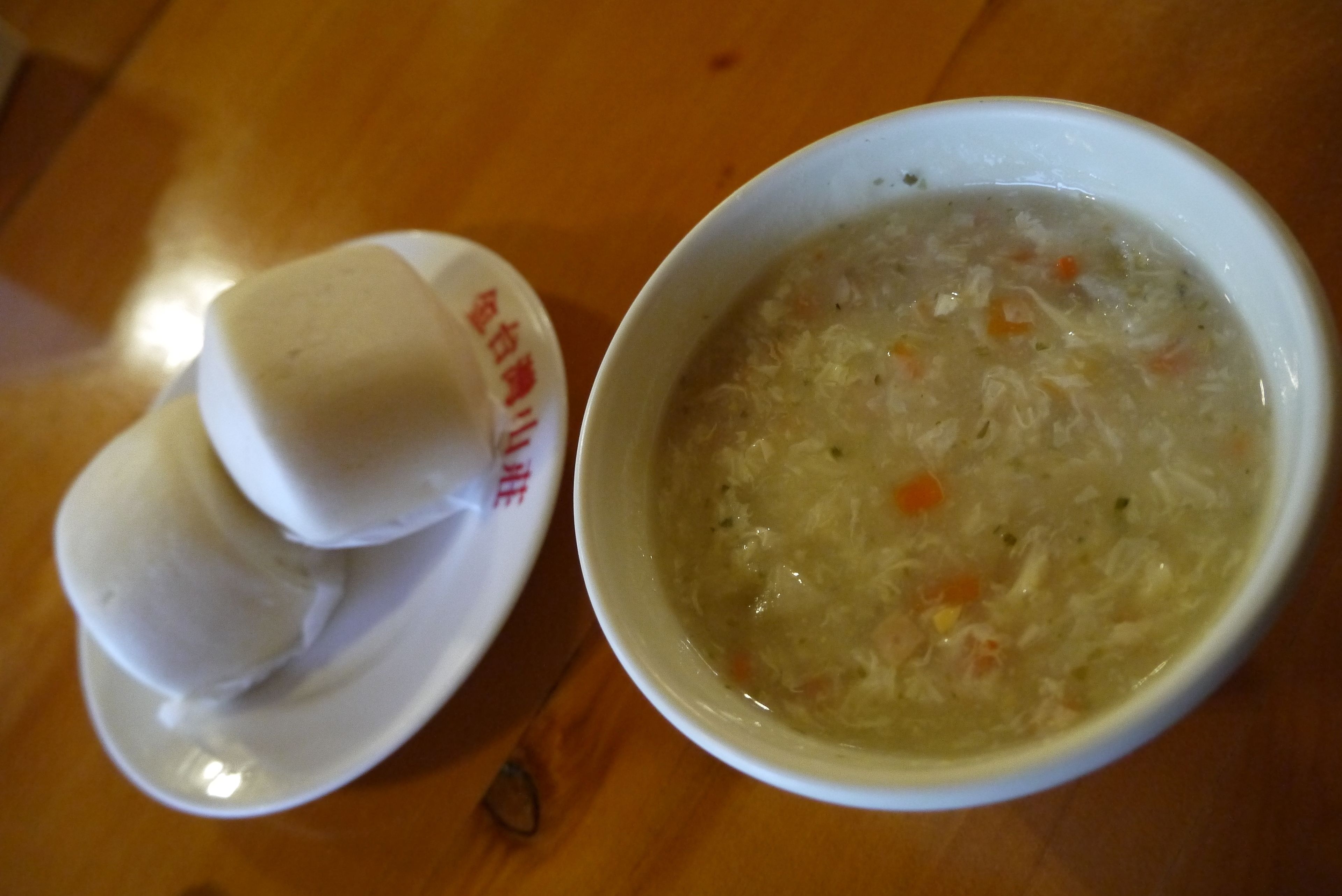 Un tazón de sopa con vegetales y un plato con dos albóndigas.