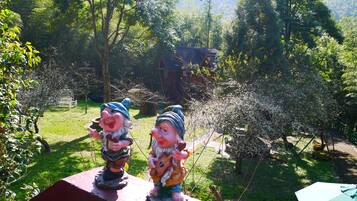 Two garden gnomes on a ledge overlooking a garden with a house in the background.