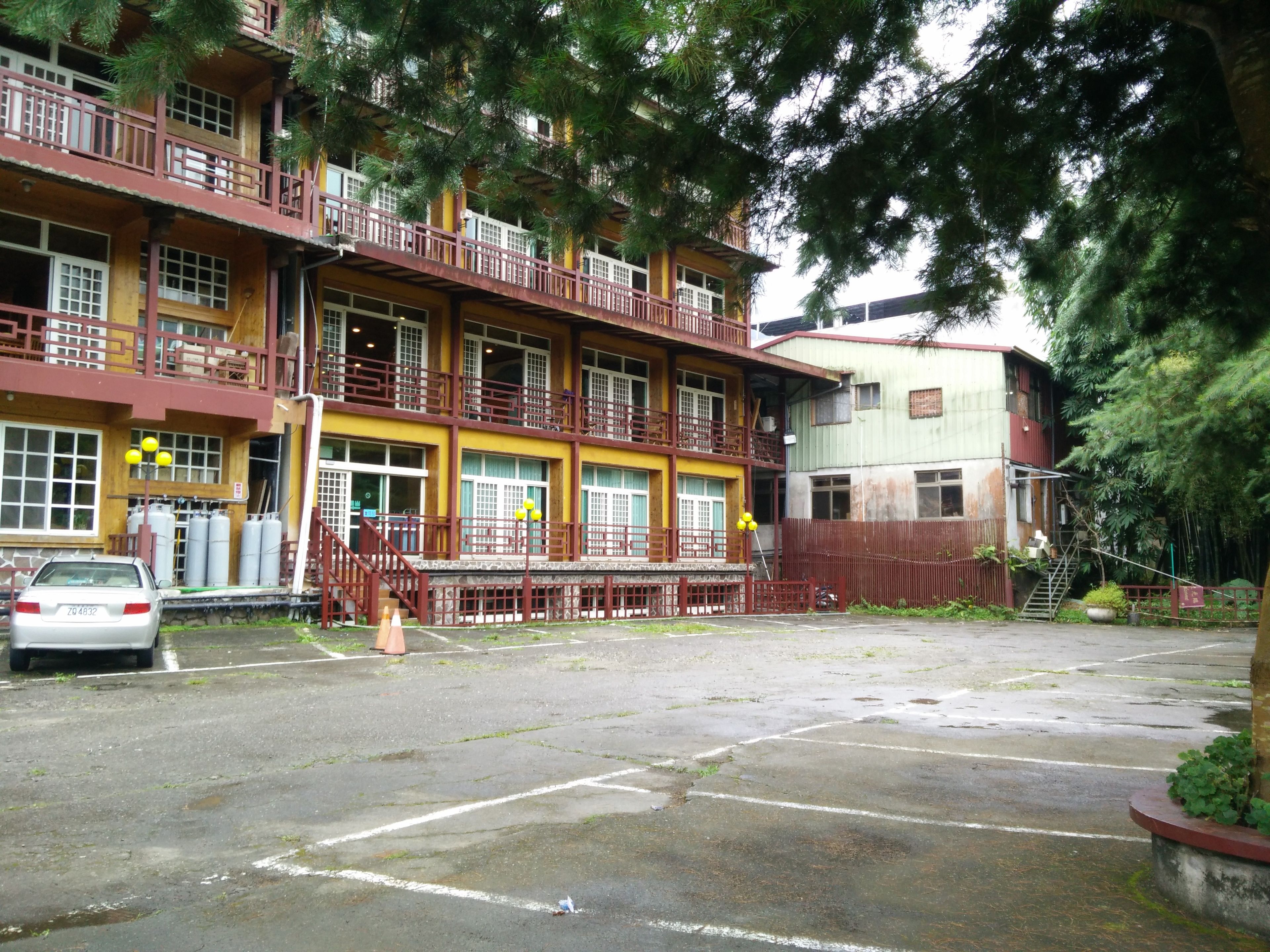 A multi-story building with balconies, a parking area, and a staircase leading to a lower level.