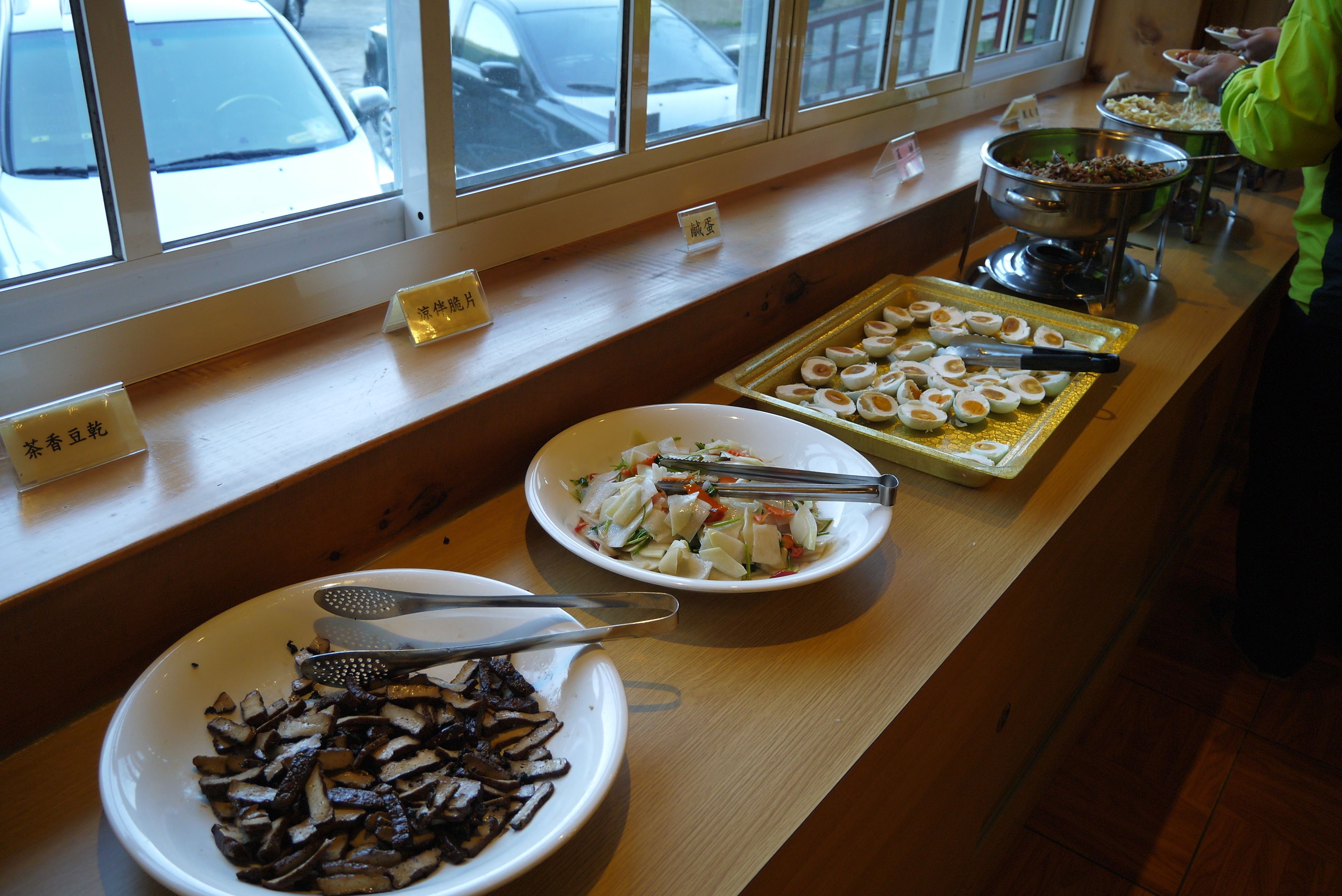 A buffet table with various dishes, including sliced mushrooms, a salad, and boiled eggs.