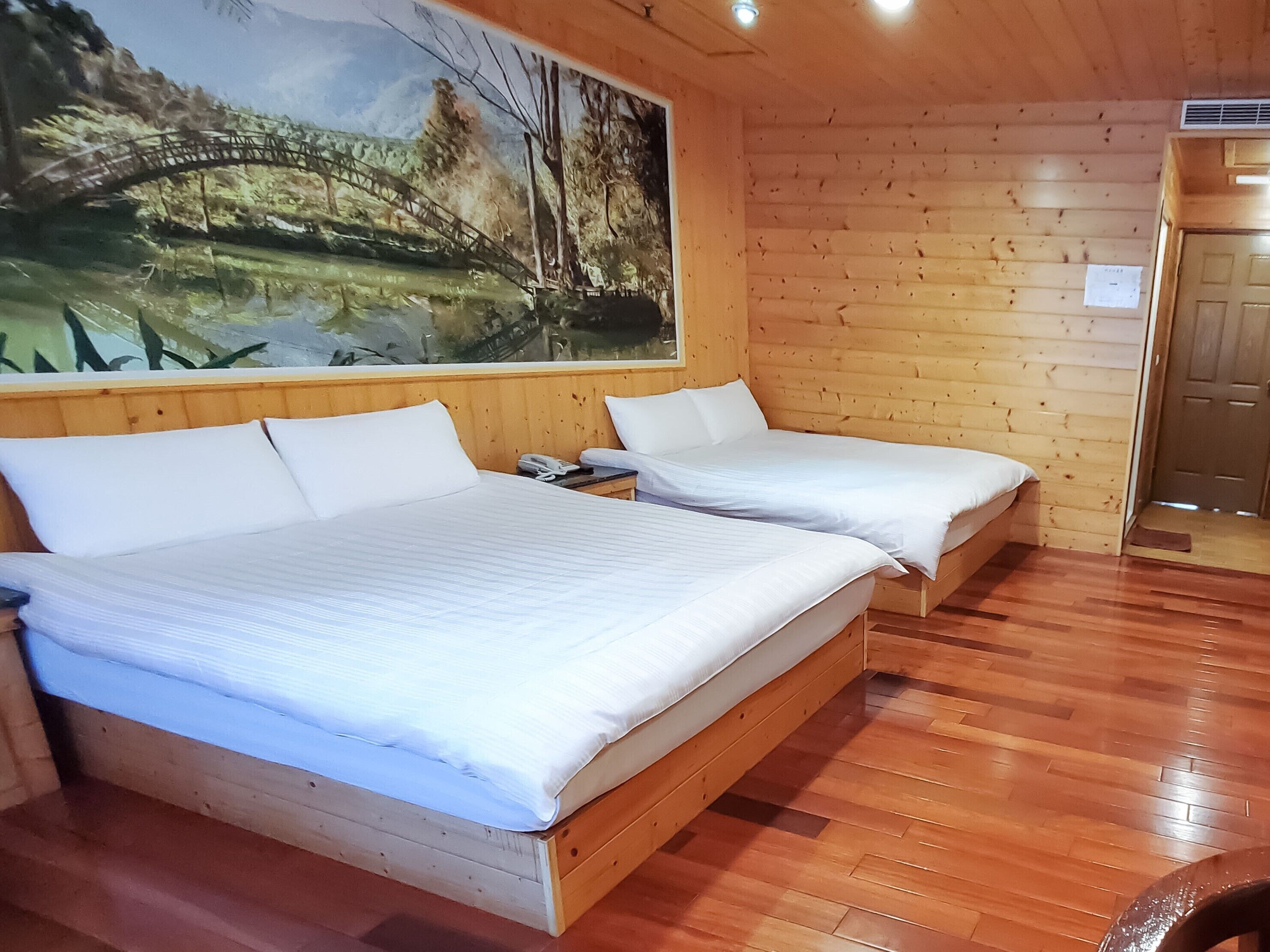 Una habitación de cabaña de madera con dos camas, un cuadro de un puente y suelo de madera.