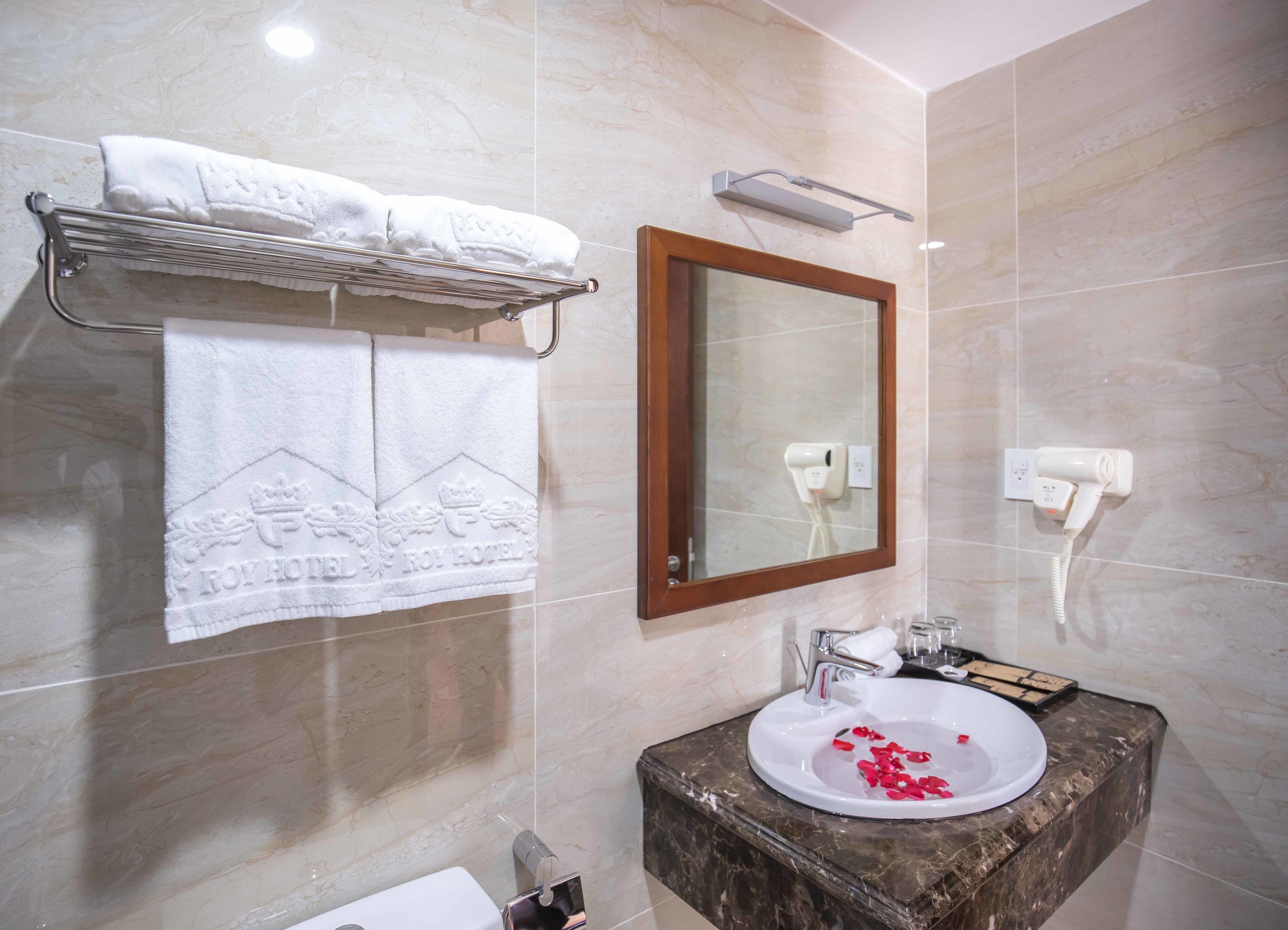 A bathroom with a marble wall, a sink with rose petals, a towel rack with towels, a mirror, and a hairdryer.