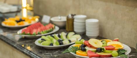 A buffet table with various fruits and vegetables, including watermelon, apples, and oranges.