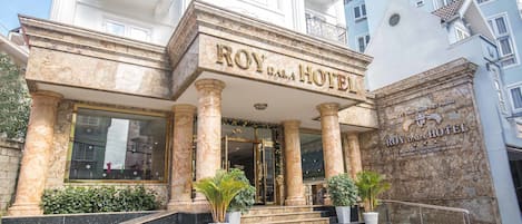 The exterior of the Roy Dalai Hotel with marble columns, a grand entrance, and a sign indicating its location in Hanoi, Vietnam.