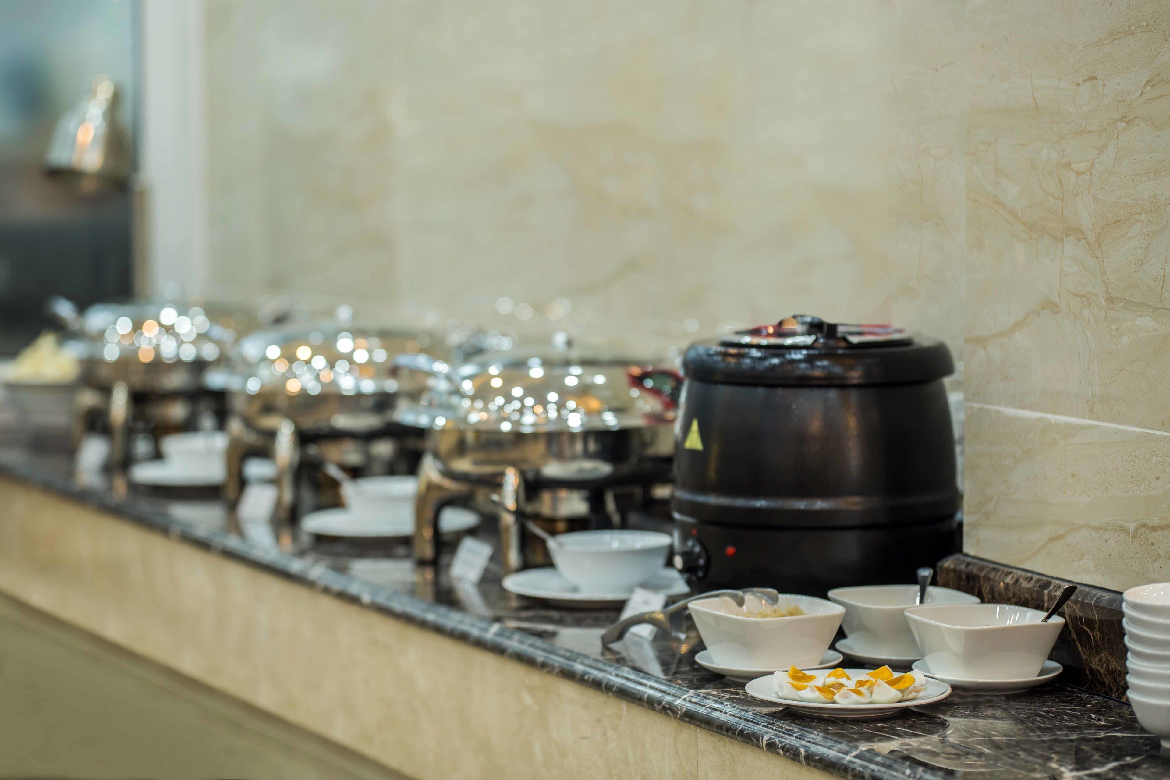 A buffet setup with various dishes and a large black container, likely for beverages, on a marble countertop.