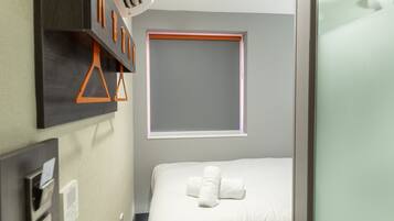 Habitación de hotel con cama, ventana, aire acondicionado instalado en la pared y un perchero para toallas.