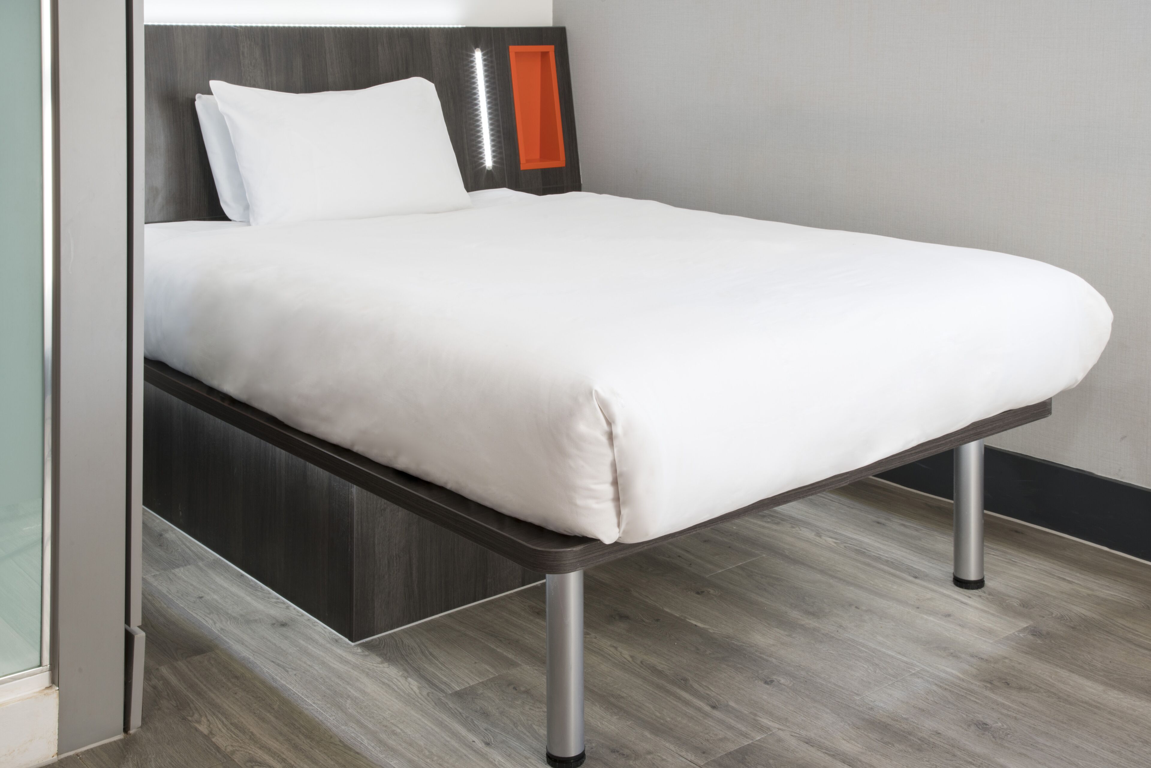 Een modern bed met een houten hoofdbord, een witte matras en metalen poten.