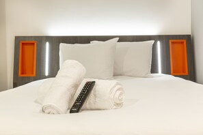 A neatly made bed with white linens, a rolled white towel, and a remote control. - easyHotel Reading (Reading)