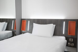 A hotel room with a large bed, a bedside table, and a mirror. There are orange accents on the wall and a light fixture above the bed. - easyHotel Reading (Reading)