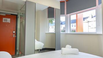 A hotel room with a bed, a mirror, a window, and a door.