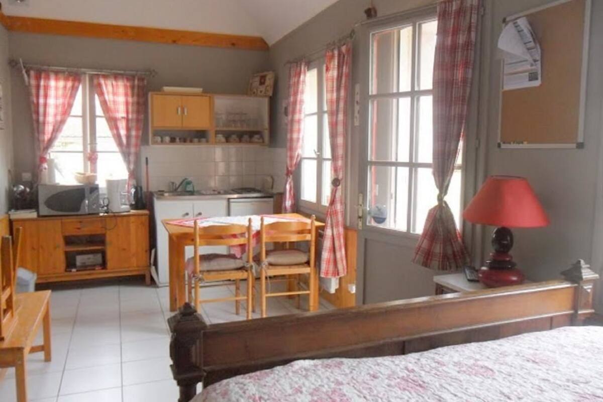 A compact room with a bed, a wooden desk, a chair, a small table, and a kitchenette.